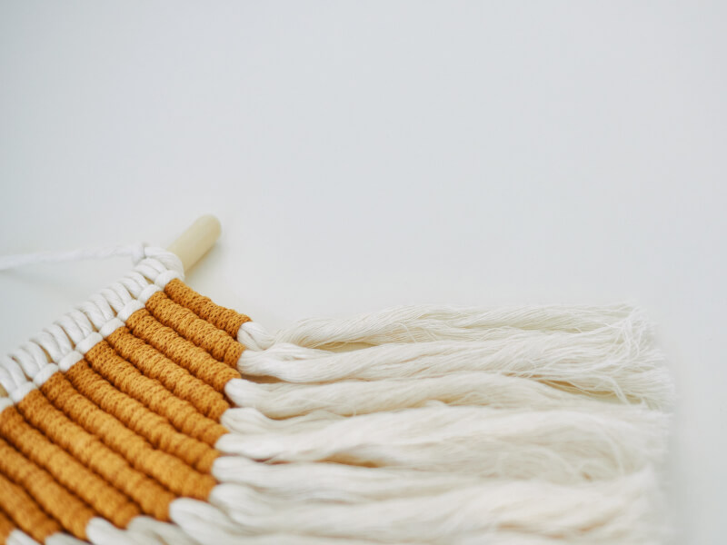 Macrame work close up in yellow and frayed white on wooden pole hanger
